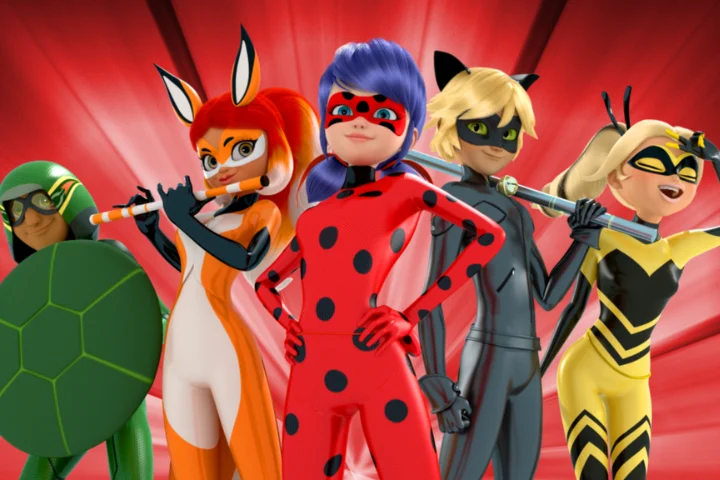 Imagem promocional com quatro super-heróis animados em poses de ação sobre um fundo vermelho com efeito de raios. No centro está uma heroína de uniforme vermelho com bolinhas pretas. Ao lado dela aparecem um herói vestido de preto com orelhas de gato, uma heroína de traje laranja e branco segurando um bastão, uma heroína em amarelo e preto sorrindo, e um personagem de verde com um grande escudo em formato de casco de tartaruga.